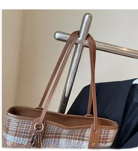 Détail de la poignée en cuir marron et du sac cabas à carreaux sur un cintre en métal