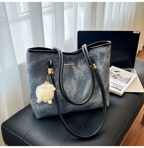 Detail of a denim tote bag with black leather trim and plush pom-pom charm on a bench