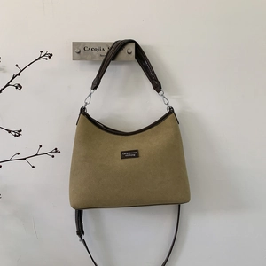 Detail of suede crossbody bag with leather trim hanging on a minimalist wall