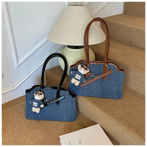 Detail of denim tote bag with leather handles and a cute teddy bear charm on stairs