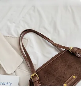 Detail view of the brown suede handbag with adjustable leather straps and metal hardware