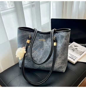 Detail of denim tote bag with black leather straps and white plush ball charm on a chair