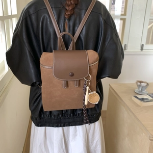 Dettaglio di zaino vintage marrone opaco con ciondolo indossato da una modella
