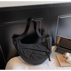 Dettaglio borsa a mezzaluna in nylon nero con cerniere intrecciate e tracolla larga