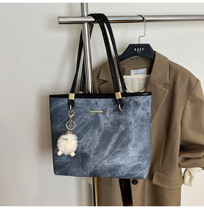 Detail of stone-washed grey tote bag with gold hardware and plush charm on a hanger