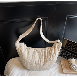 Dettaglio della borsa a mezzaluna plissettata bianco crema con elementi lifestyle