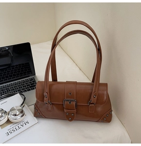 Detail of vintage brown baguette bag with metal rivets and large buckle on a desk