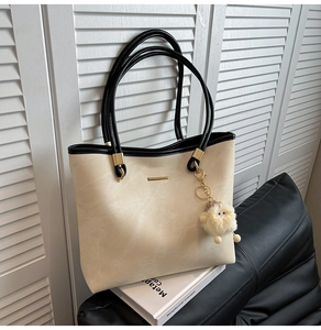 Detail of cream tote bag with black handles, gold hardware, and a plush lamb charm