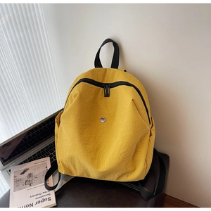 Zaino minimalista in nylon giallo brillante accanto a un laptop e un libro sul tavolo