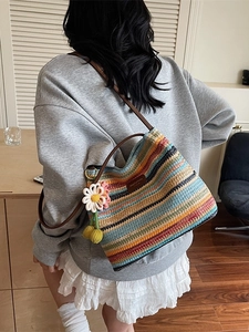 Bunte gestreifte Strick-Eimertasche mit Blumenanhänger und Ledergurt am Modell