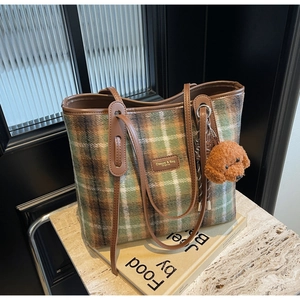 Detail of green plaid wool tote bag featuring a brown teddy bear charm and leather straps