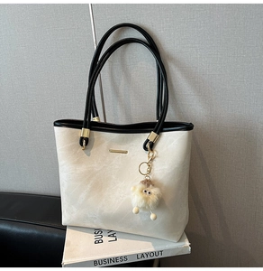 Detail of beige tote bag with black straps, gold hardware and plush sheep charm decoration