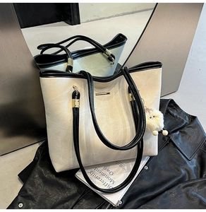 Detail view of cream tote bag with black trim and plush charm on a leather jacket