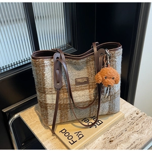 Detail of plaid wool tote bag with brown leather handles and a plush dog charm