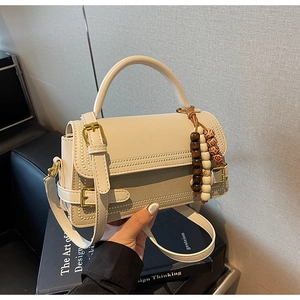 Detail of beige faux leather handbag with wooden bead pendant and crossbody strap