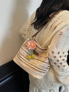 Gestreifte Stroh-Eimertasche mit Lederriemen und Blumenanhänger an einem weiblichen Model