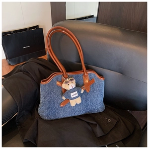 Detail of blue denim tote bag with brown faux leather handles and teddy bear charm