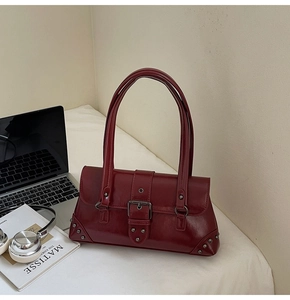 Macro detail of wine red patent leather bag with metal buckle and rivets on the desk