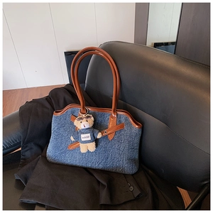 Detail of blue denim tote bag with brown leather trim and cute teddy bear charm