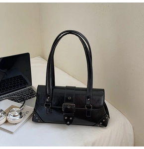 Detail of black vintage leather tote with silver rivets and buckle in a workspace setting