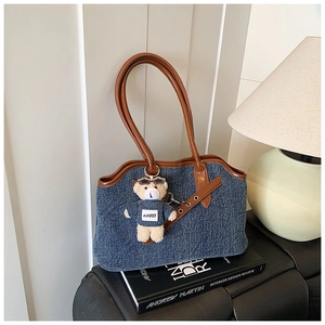 Detailed view of denim tote bag with brown faux leather trim and cute bear plush pendant
