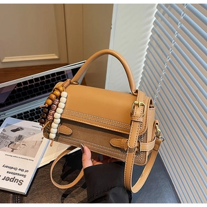 Close-up of vintage brown crossbody bag featuring metallic buckle and beaded pendant detail