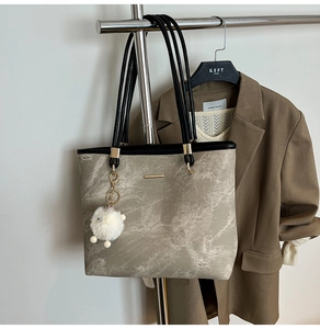 Detail of grey marble pattern tote bag with gold logo plate hanging on a metal rack
