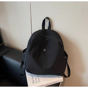Dettaglio di uno zaino in nylon nero con logo M in metallo su divano in pelle