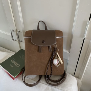 Dettaglio dello zaino vintage in pelle marrone con ciondolo da baseball e cuciture a contrasto