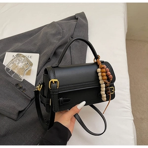 Detail of a black leather handbag with gold buckle and ethnic beaded tassel charm