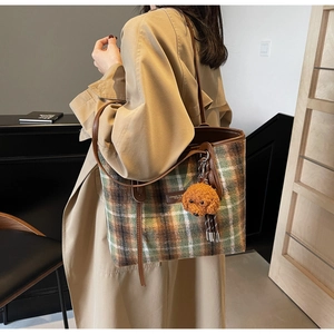 Detail of plaid wool tote bag with leather straps and a plush poodle charm pendant