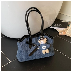 Detail der blauen Denim-Tragetasche mit schwarzem Lederbesatz und Bärenanhänger