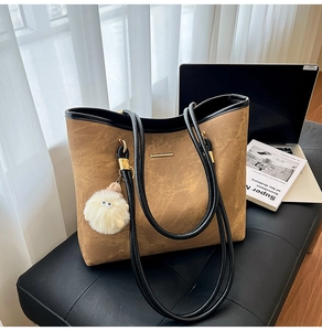 Brown large capacity tote bag with fuzzy charm and sleek gold bar detail on black bench