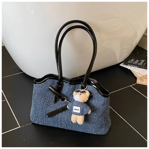 Detail of blue denim tote bag with black patent leather trim and a cute teddy bear charm