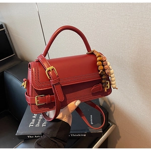 Detail of red leather crossbody bag with golden buckle and beaded wooden charm