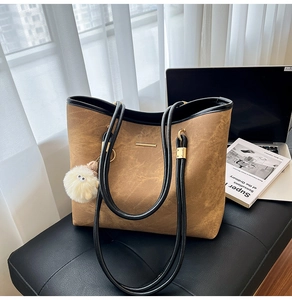 Brown leather tote bag with black straps and white plush pendant for daily commute