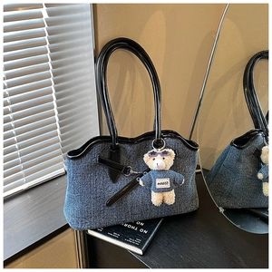 Detail of blue denim tote bag with black glossy handles and a cute plush bear charm