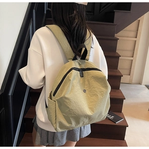 Dettaglio di uno zaino in nylon verde chiaro con un logo metallico rotondo e minimalista