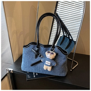 Detail view of denim tote bag with black glossy leather trim and cute teddy bear charm