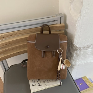 Dettaglio zaino vintage in pelle scamosciata marrone con patta e ciondolo da baseball