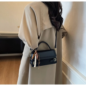 Detailed side view of a black vintage crossbody bag with wood bead tassel on a trench coat