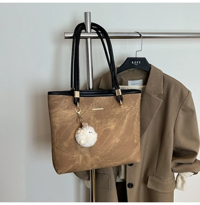 Brown tote bag with plush ball charm hanging on a rack for a stylish commute look