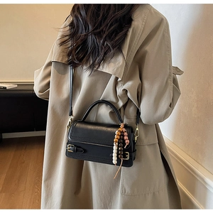 Detail of a vintage black leather crossbody bag with decorative bead charm and strap
