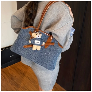 Detail of blue denim tote bag with brown leather trim and cute teddy bear charm accessory