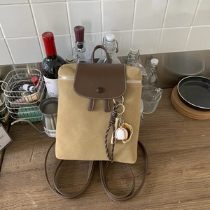 Dettaglio dello zaino vintage kaki opaco con patta in pelle marrone e ciondolo baseball