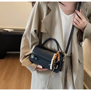 Detail of a vintage black matte crossbody bag with retro bead pendant and metal buckle
