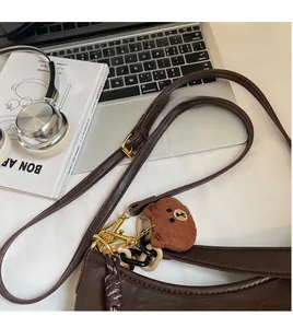 Detail of dark brown leather shoulder bag with plush charm and adjustable strap