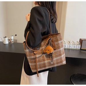 Detail view of large checkered wool tote bag with brown leather strap and teddy bear charm