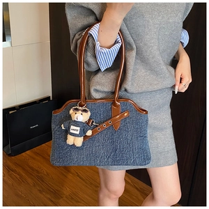 Close-up of denim tote bag with brown leather straps and cute plush bear accessory