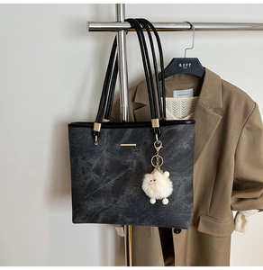 Detail of black marble textured tote bag with golden metal trim and plush charm